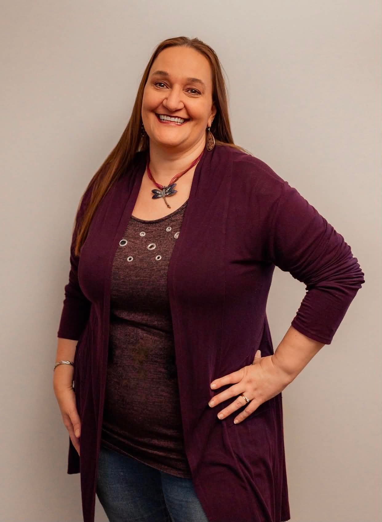 A portrait of Gina smiling and standing with a hand on her left hip.