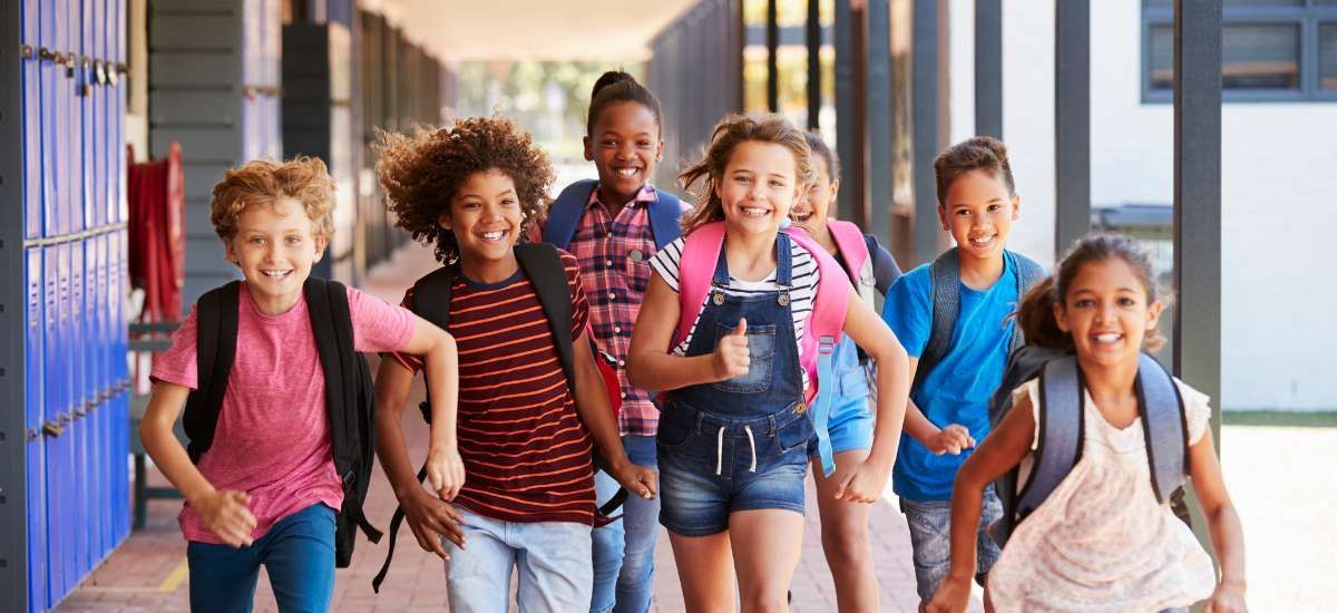 Cheerful group of students running down the hallway with backpacks on.
