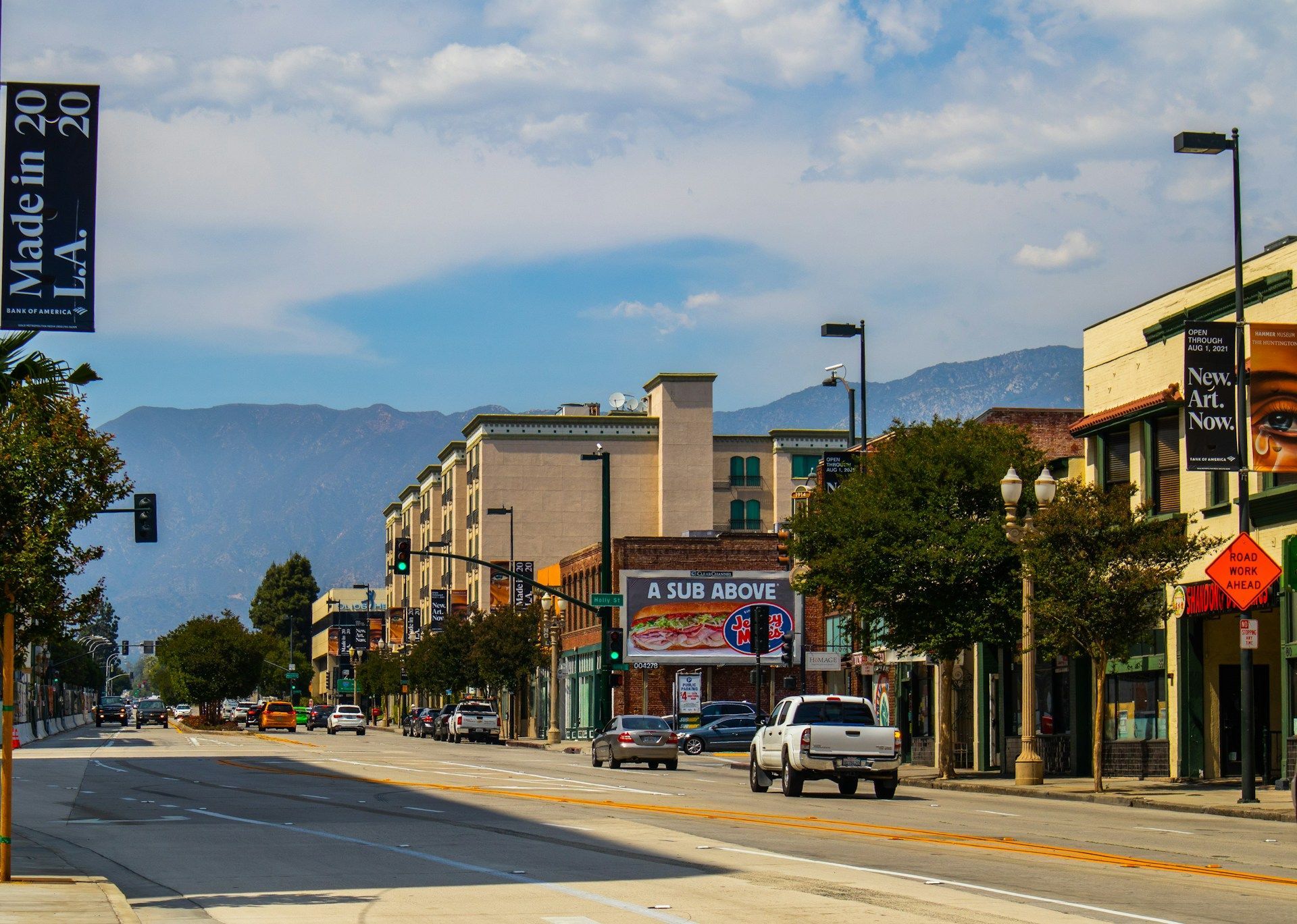 A street scene in Pasadena, California, featuring buildings, streetlights, a pickup truck, and mountains in the distance.