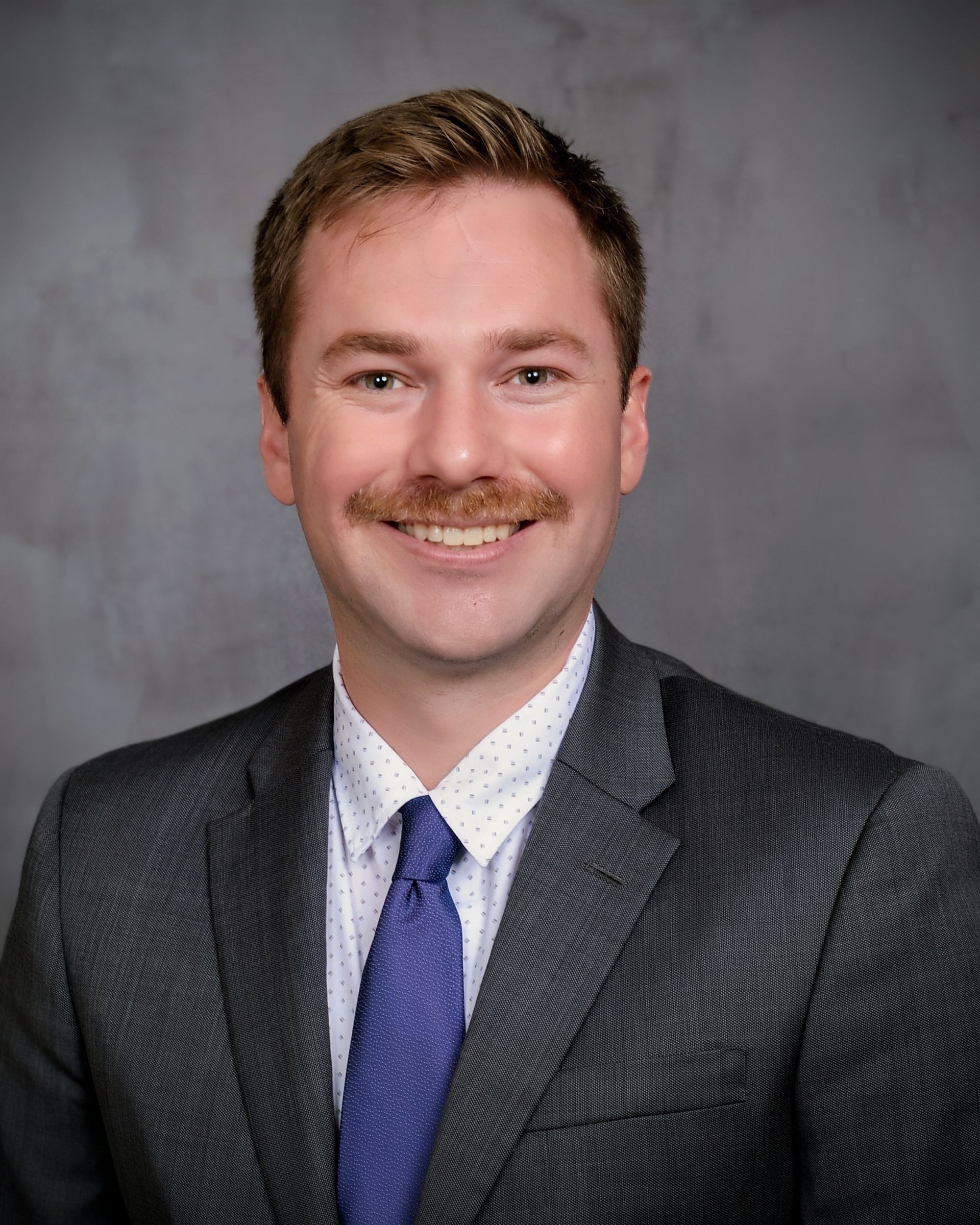 A man with a beard is wearing a white shirt and smiling for the camera.