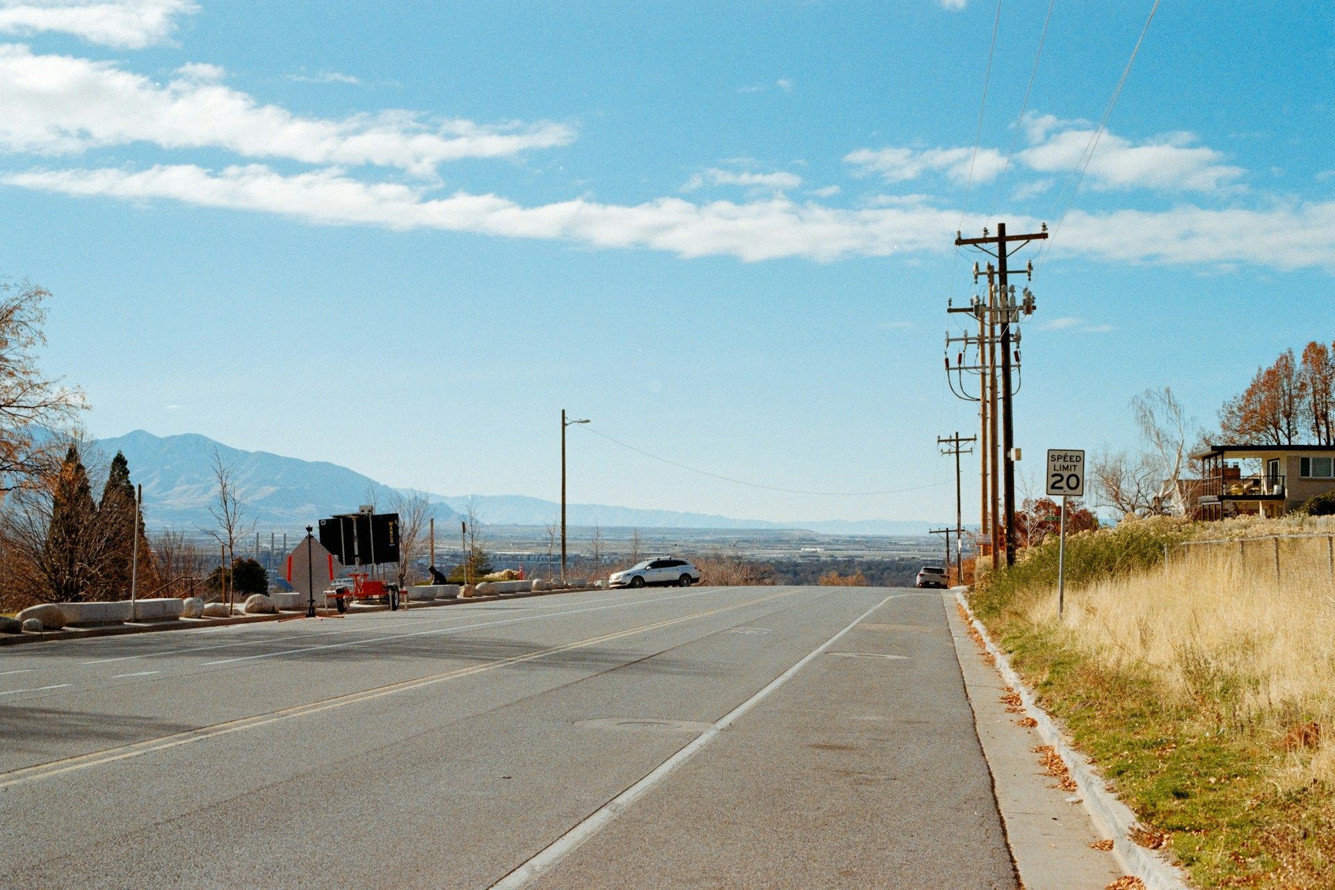 A paved road leads toward a mountain view under a blue, partly cloudy sky with power lines on the right.