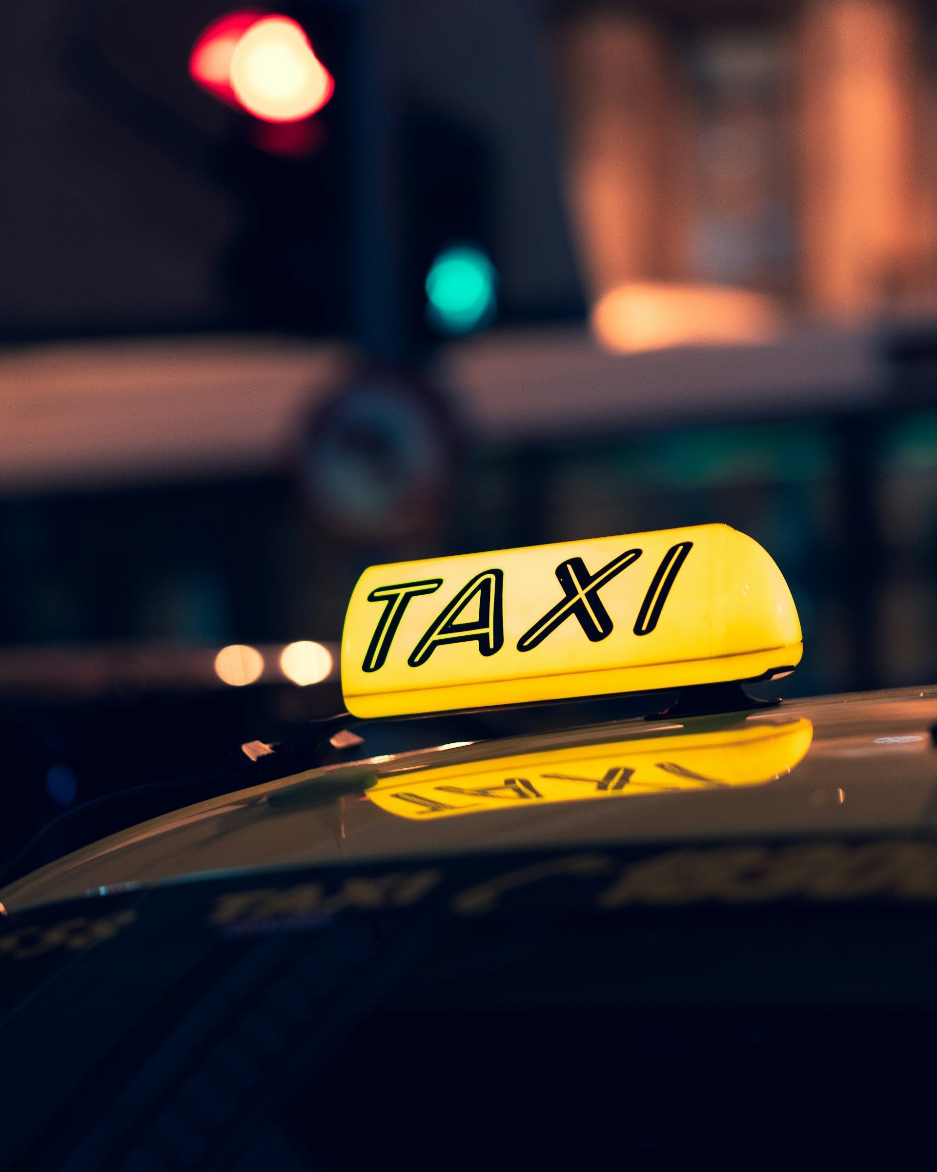 A yellow taxi sign mounted on the roof of a vehicle at night, with blurred city lights in the background.