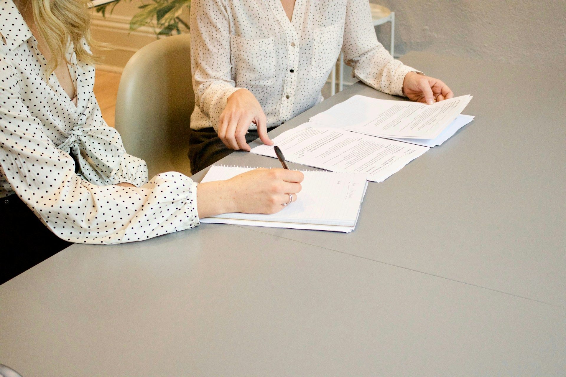 Two people in polka-dot shirts sit at a table reviewing documents, with one person writing on a paper.