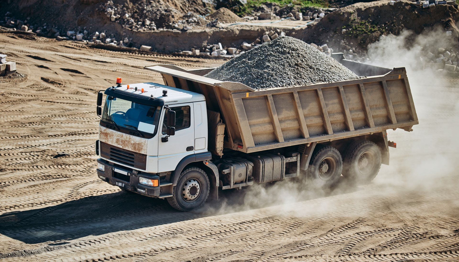 Dump truck driving on a dirt construction site carrying a large load of gravel.