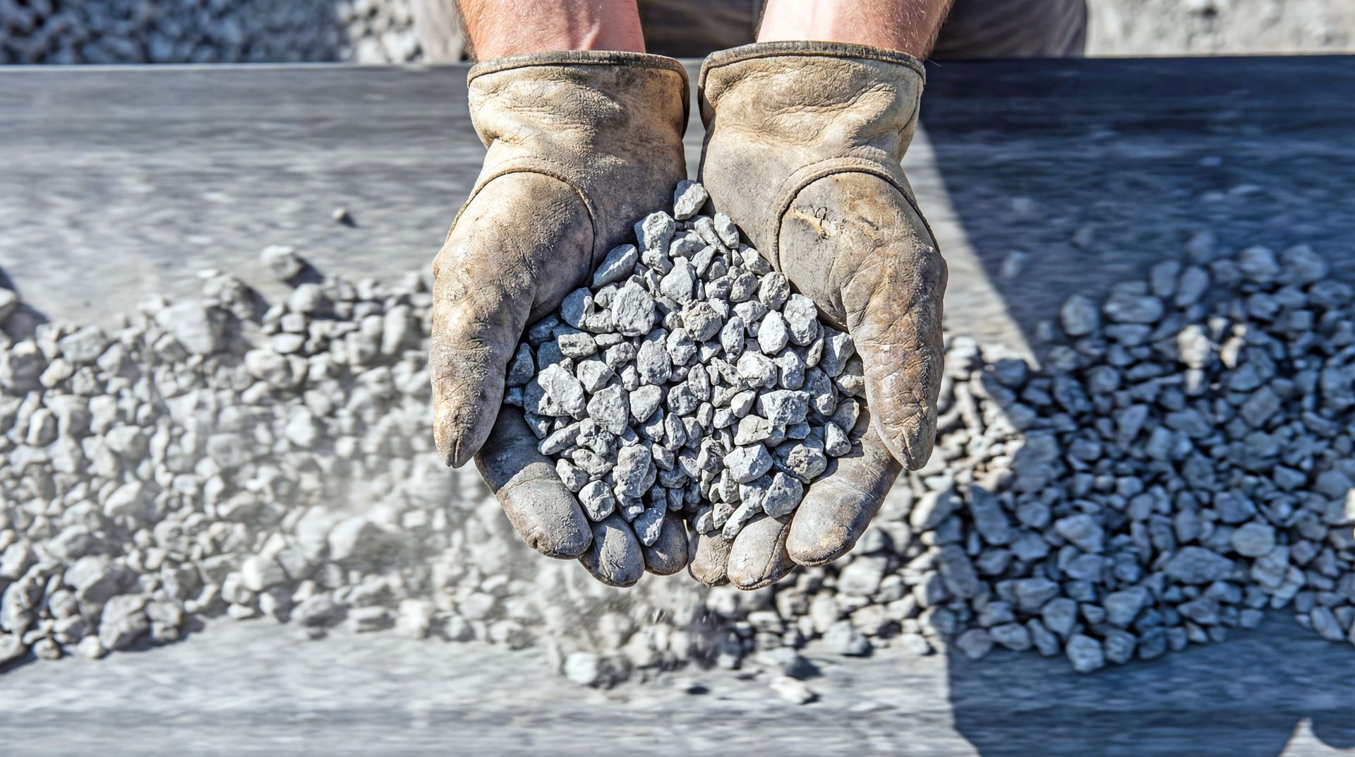 Gloved hands holding a pile of small gravel stones at a construction site.
