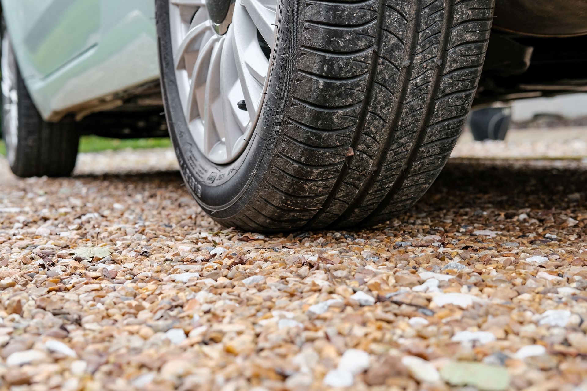 Close-up of a car tire on a gravel driveway surface.