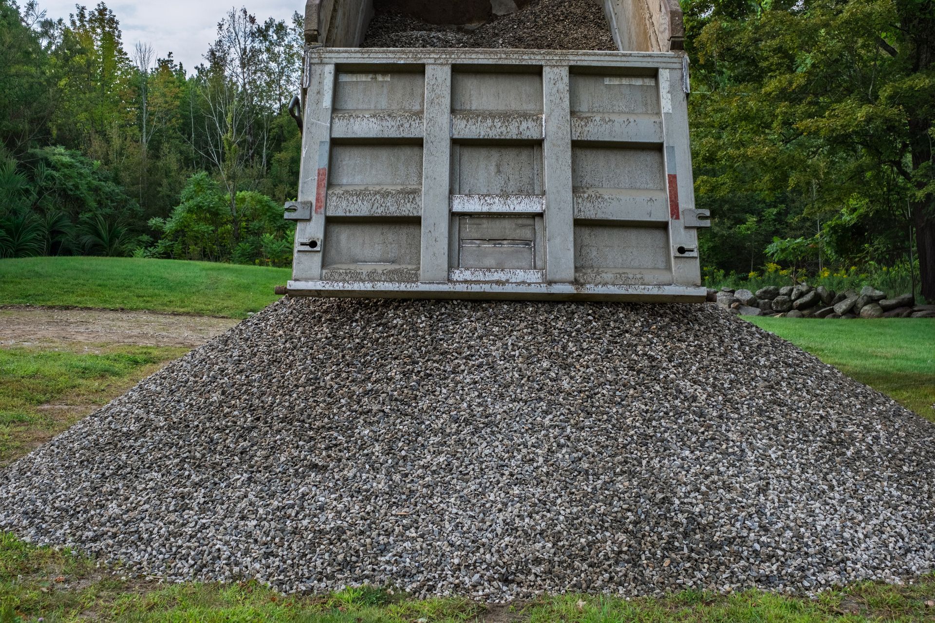 Dump truck unloading a large pile of gravel onto a grassy area for landscaping work.
