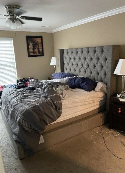 A bedroom with a bed , nightstand , lamp and ceiling fan.