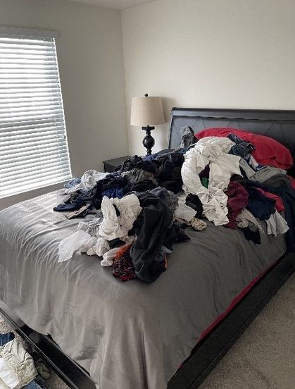A bedroom with a bed covered in clothes and a lamp.