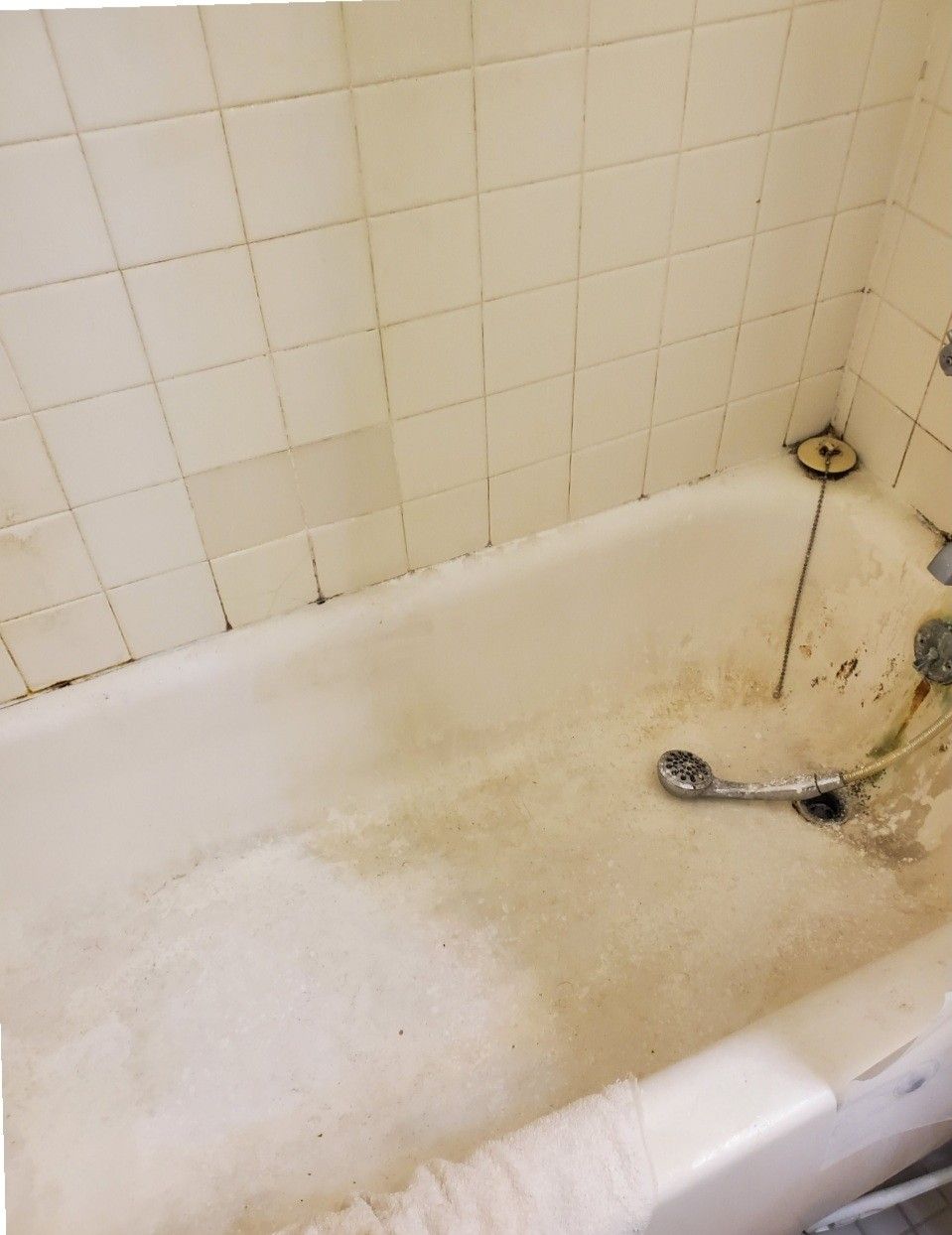 A bathtub in a bathroom with white tiles and a shower head.