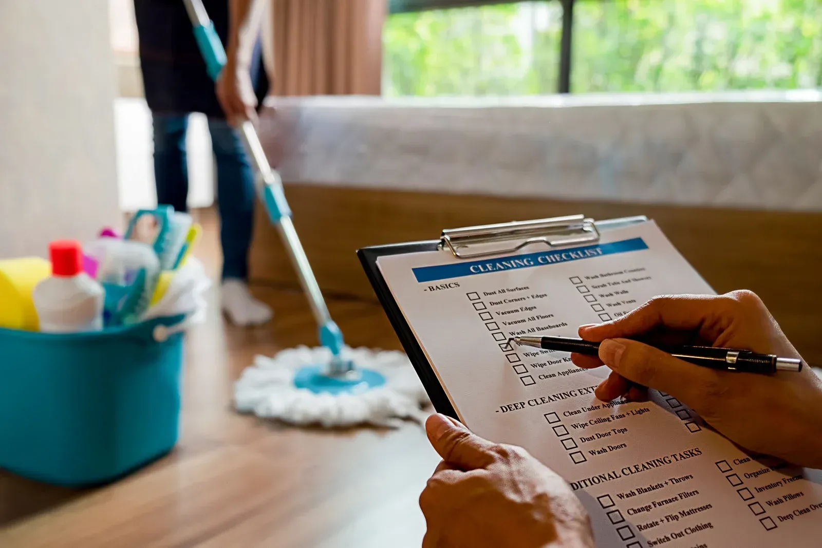 A person is writing on a clipboard while a maid is mopping the floor.