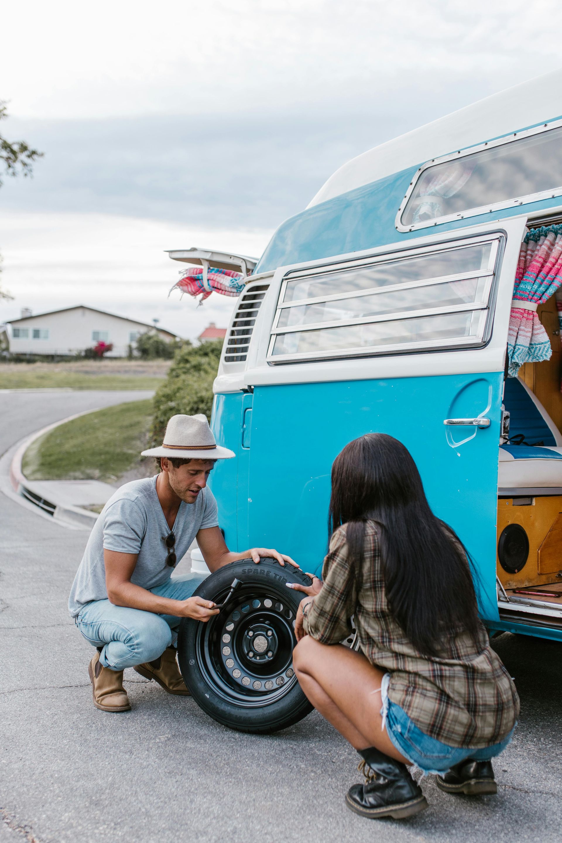 A man and a woman are changing a tire on a blue van.