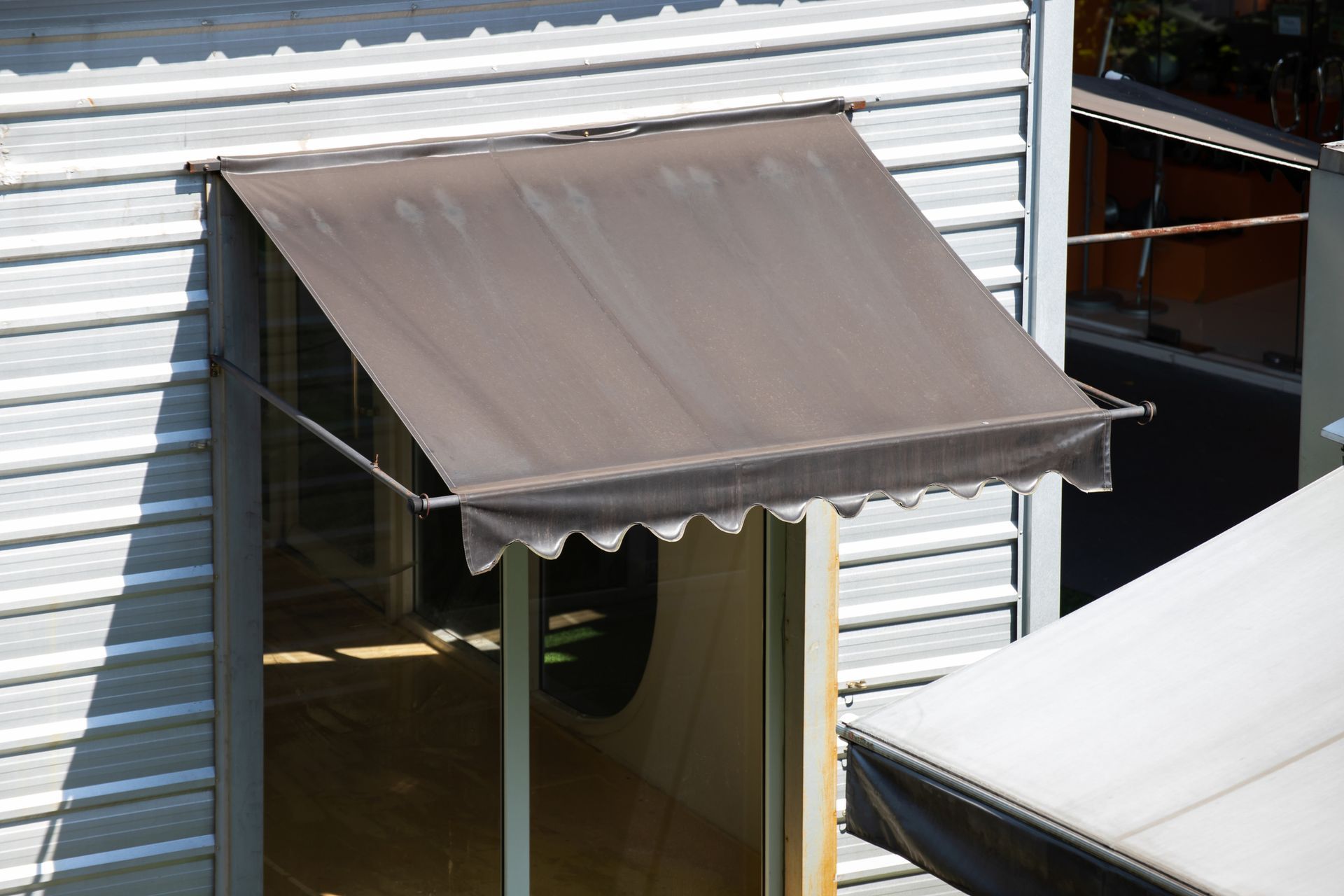 Brown retractable awning over a window leading to the interior of a building with white siding.