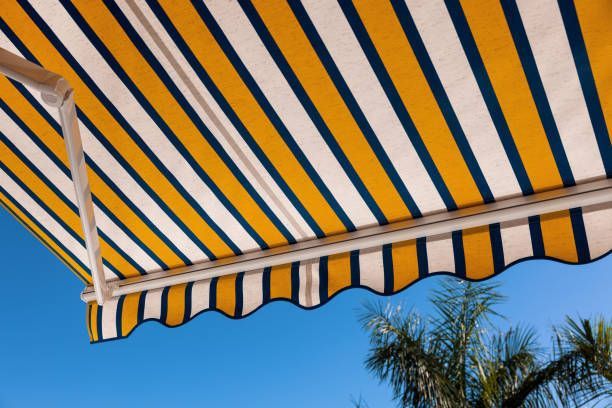 Close-up of a yellow and blue striped fabric residential awning against blue sky. — Hermantown, MN — Minnesota Awnings