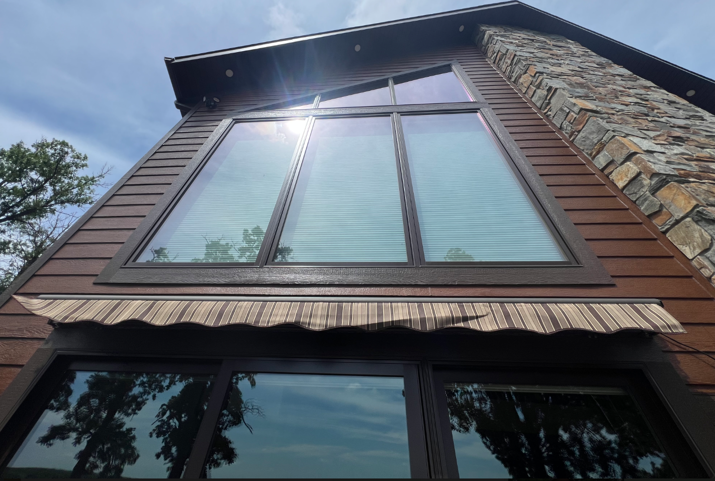 Exterior of a cabin with large windows, wood siding, and stone chimney against a bright blue sky.