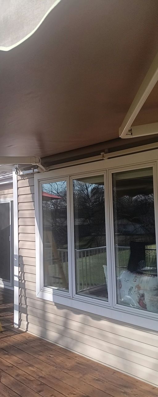 White exterior wall with horizontal siding and large windows, viewed from a wooden deck under a covered patio area.