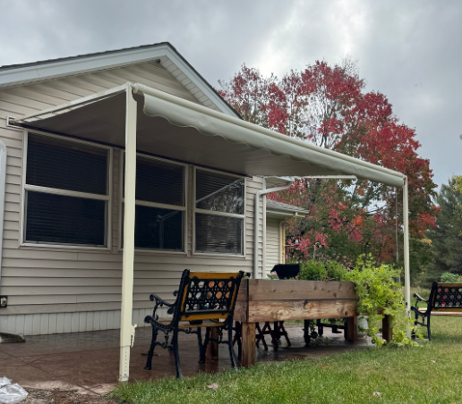 Patio with white awning, outdoor seating, wooden planter, and autumn foliage. Overcast sky.