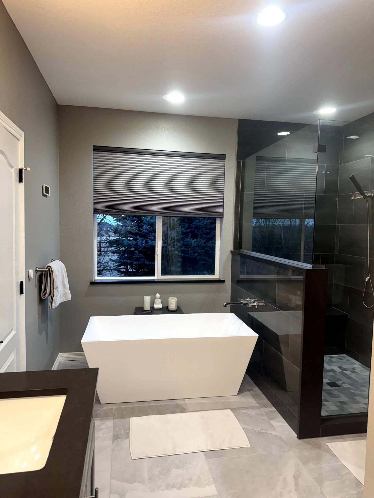 Modern bathroom with a white tub, large shower, and patterned window shade.