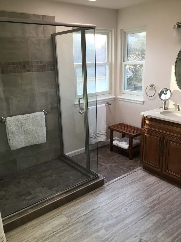 A bathroom with a walk in shower , sink , mirror and window.