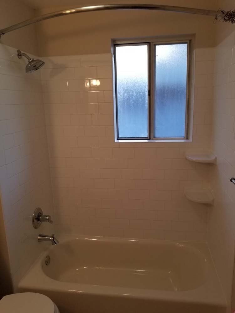 A bathroom with a tub , toilet , shower and window.