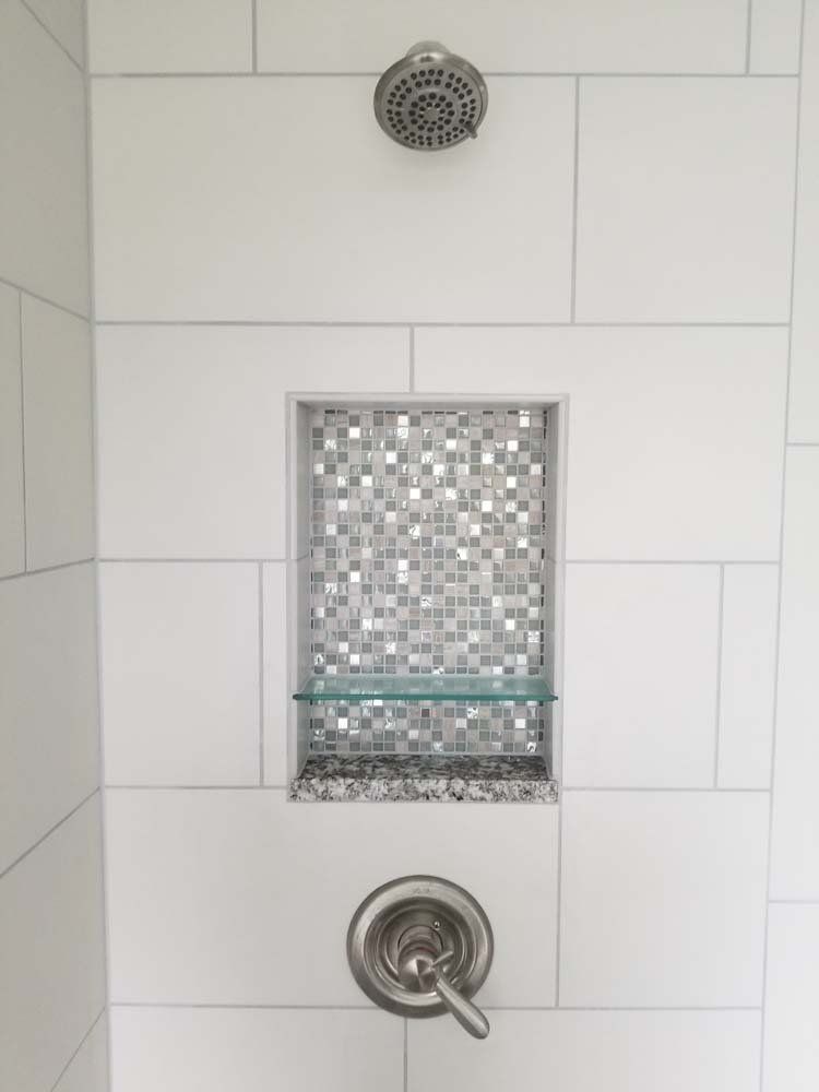 A shower with a shower head and a shelf in the corner.