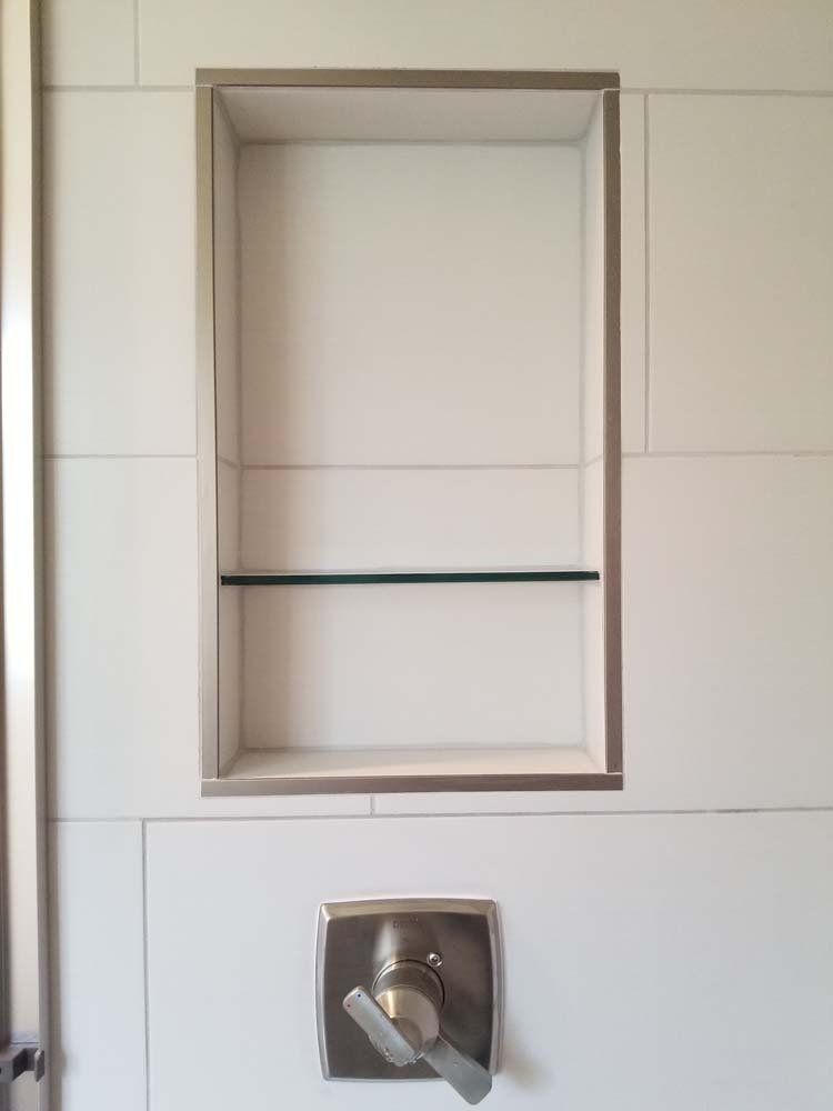 There is a shelf in the shower with a glass shelf.