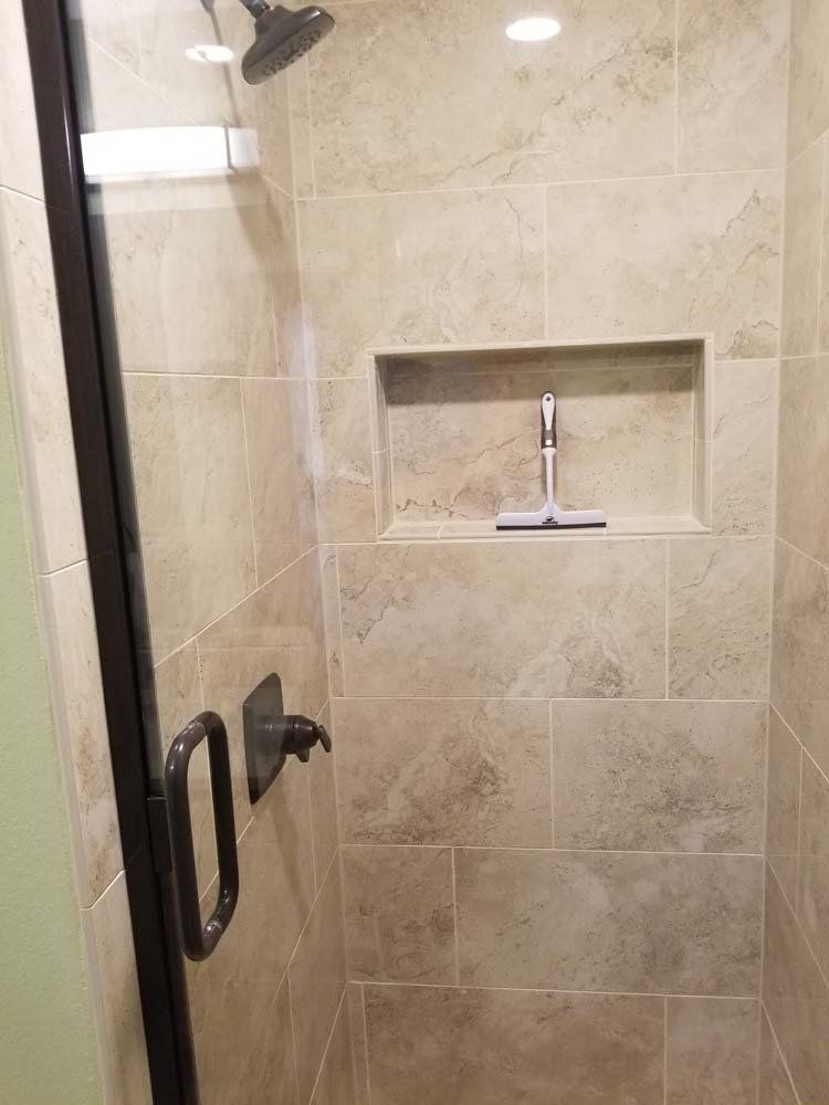 A shower with a glass door and a shelf in the wall.