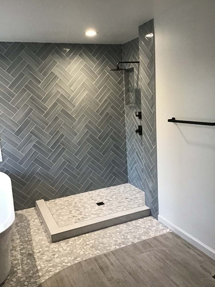 A bathroom with a walk in shower and a herringbone tile wall.