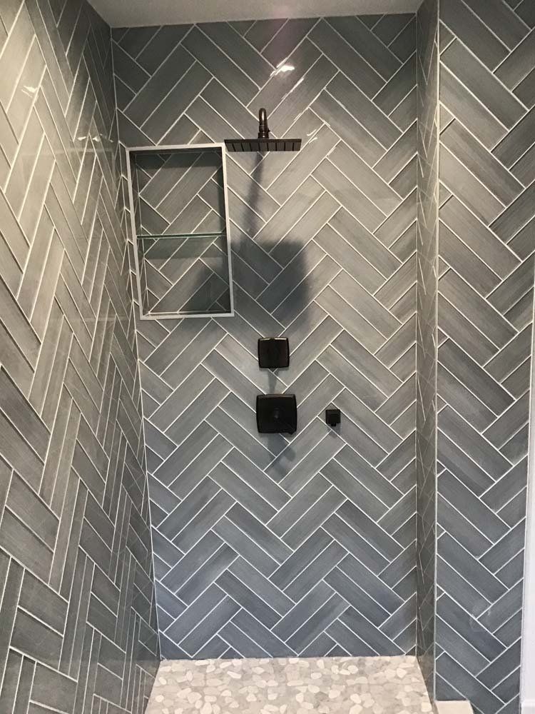 A bathroom with gray tiles and a shower with a herringbone pattern.