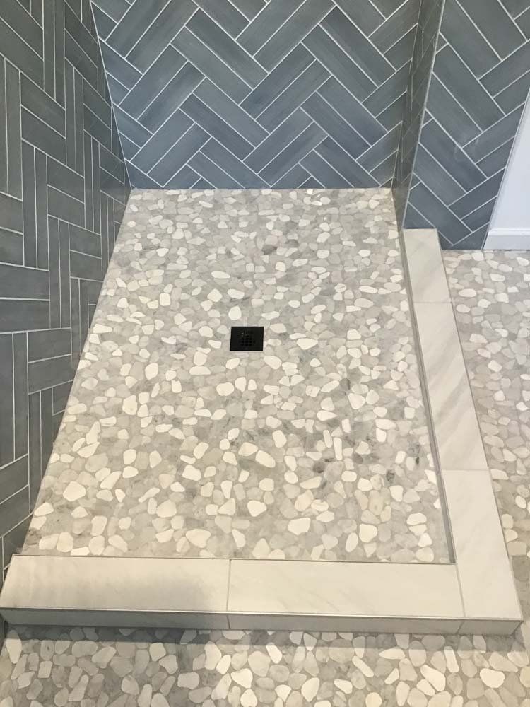 A shower stall with a herringbone pattern and a black drain.