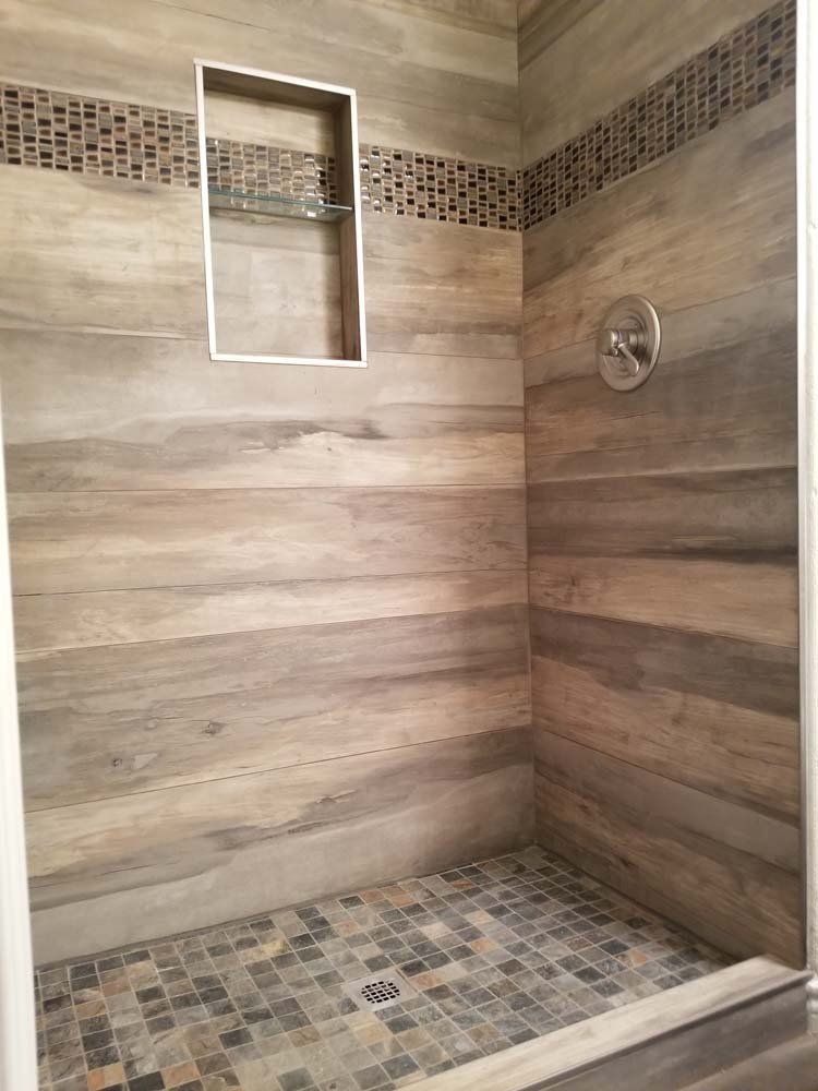 A walk in shower with wooden tiles and a mosaic floor.