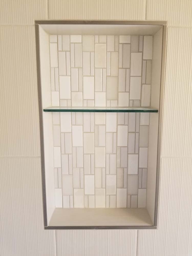 A shower niche with a glass shelf in a bathroom.