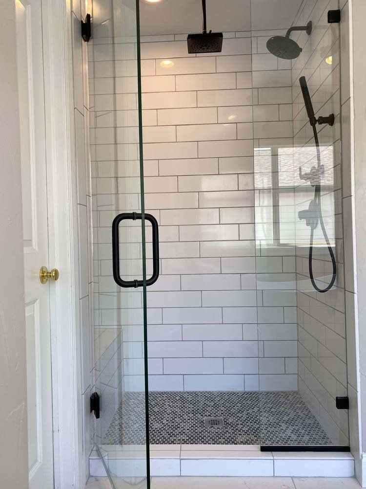 A bathroom with white tiles and a walk in shower with a glass door.