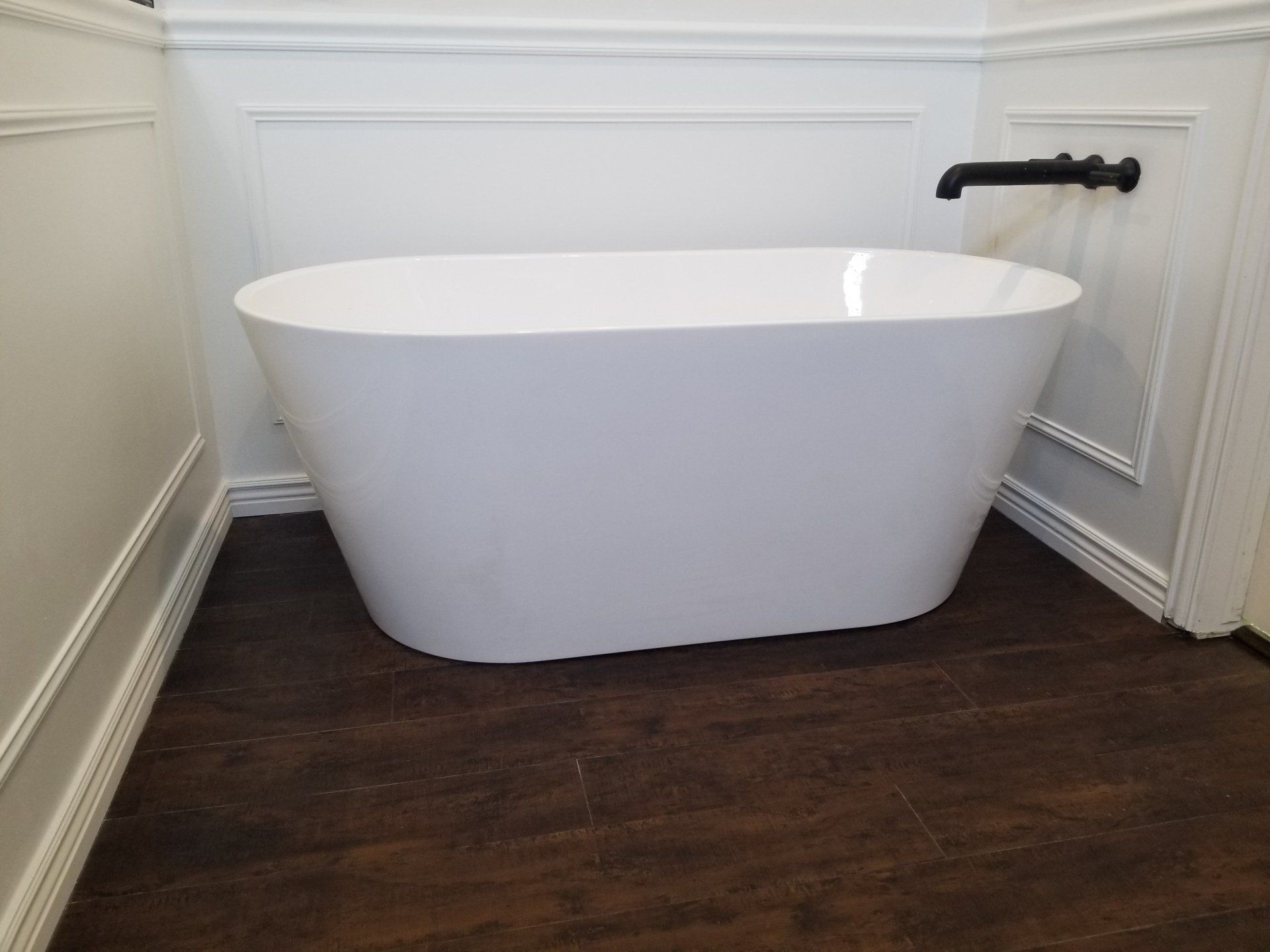 A white bathtub is sitting on a wooden floor in a bathroom.