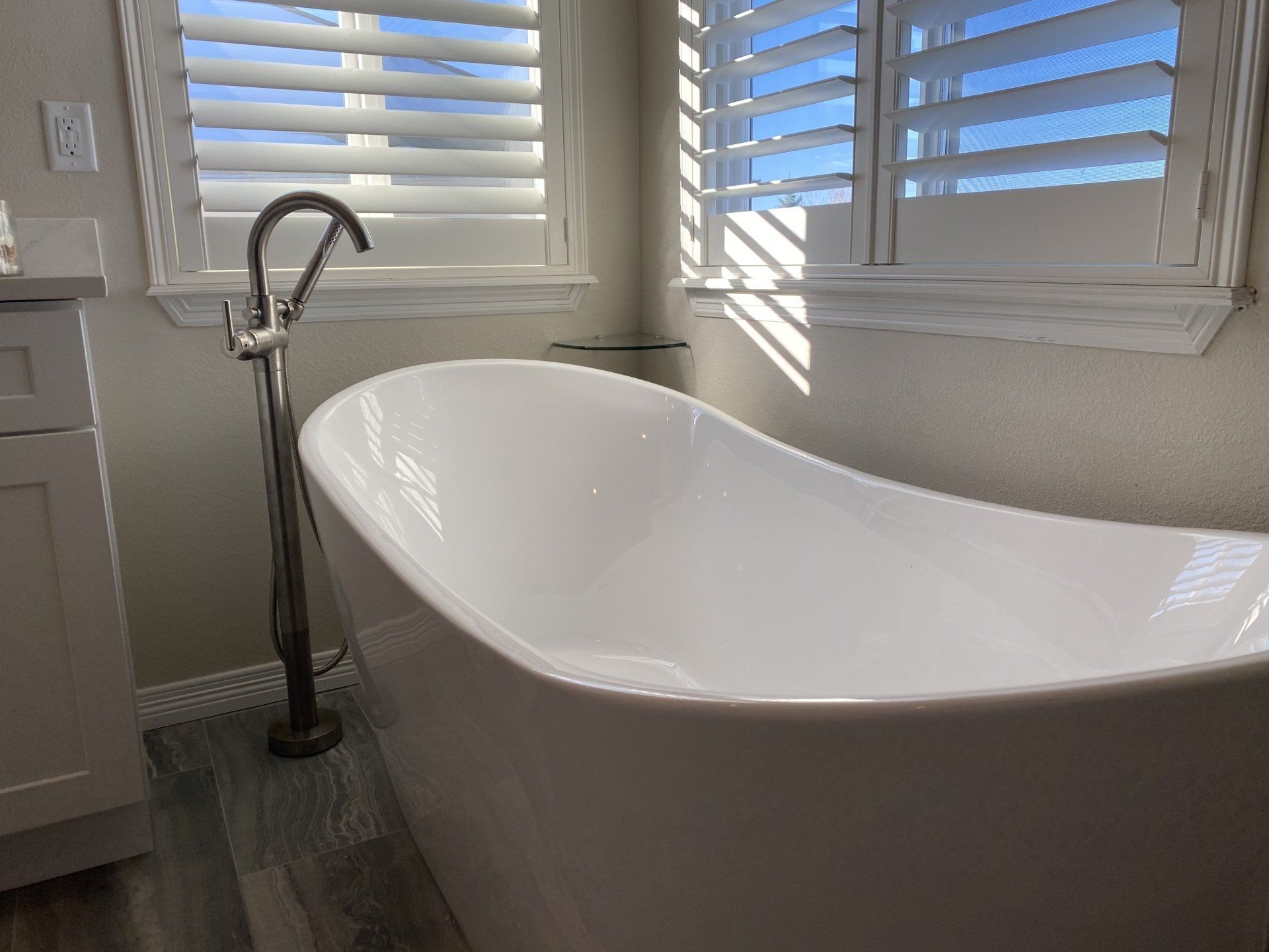 A white bathtub is sitting in a bathroom next to a window with shutters.