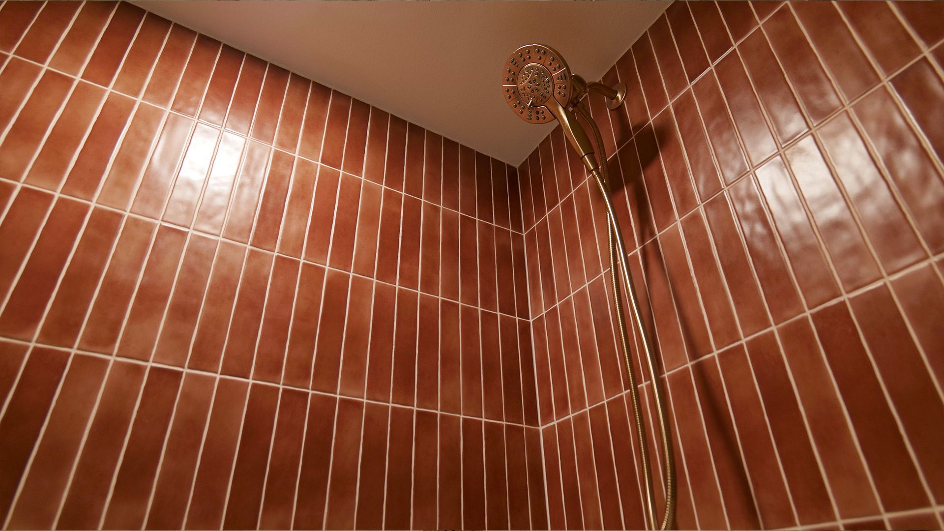 Brown tiled shower with a gold showerhead and hose.