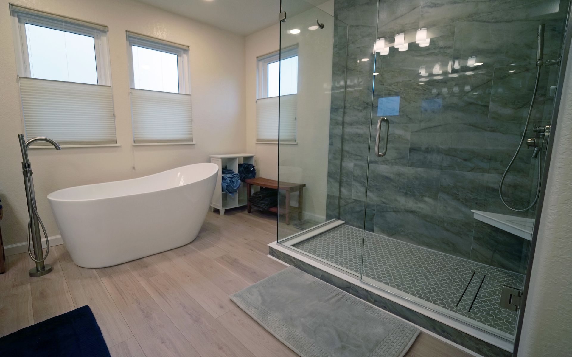 Modern bathroom with a freestanding tub, glass shower, and light wood flooring.