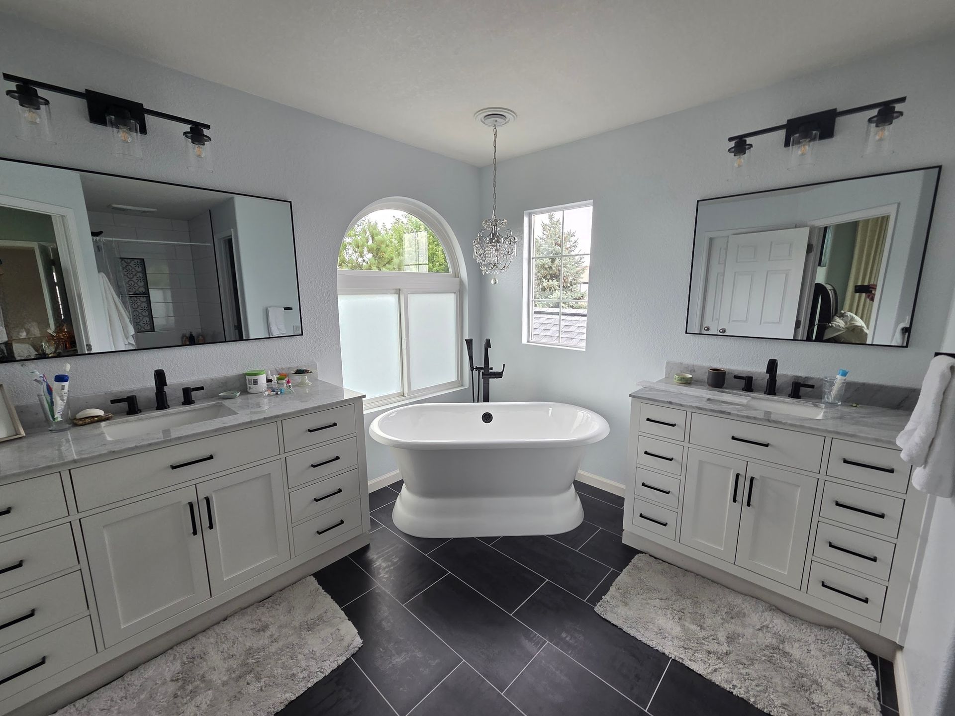 Bathroom with white vanities, black tiled floor, and freestanding bathtub.