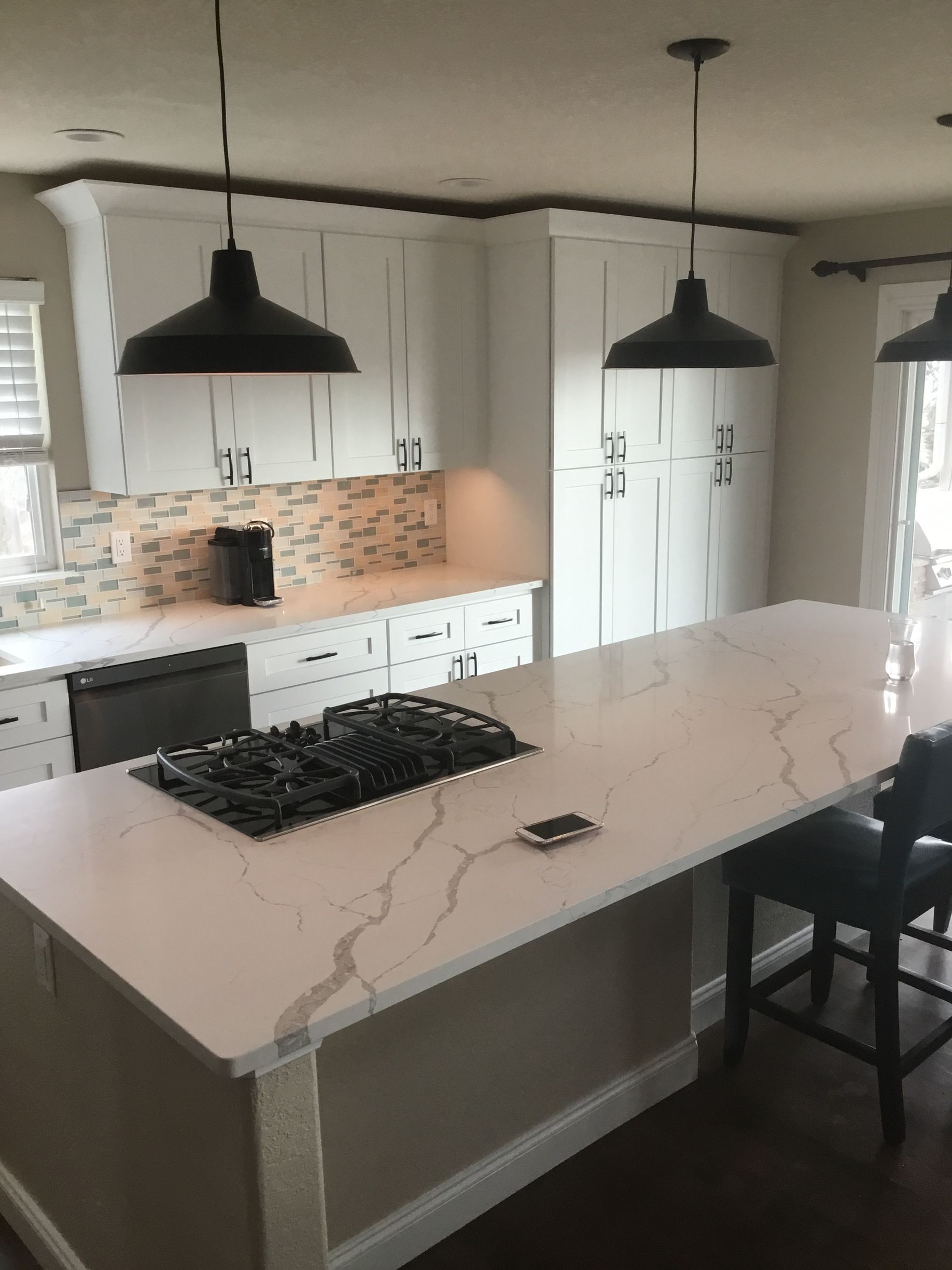 A kitchen with white cabinets and a large island with a stove top oven.