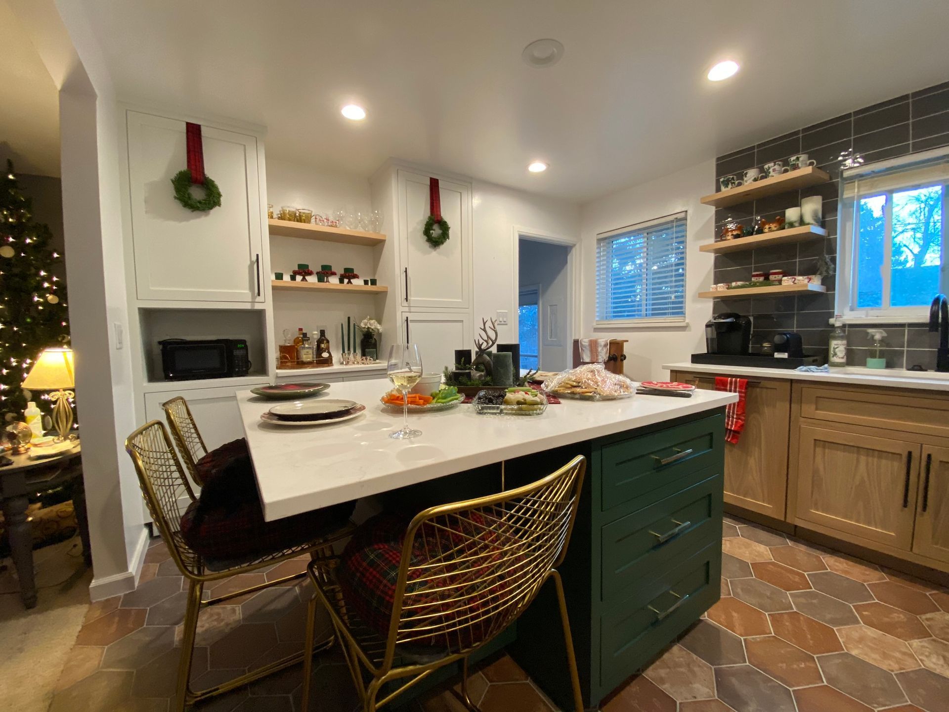 Kitchen with island and chairs, decorated for the holidays. Cabinets are white and wood-toned, with dark green island.