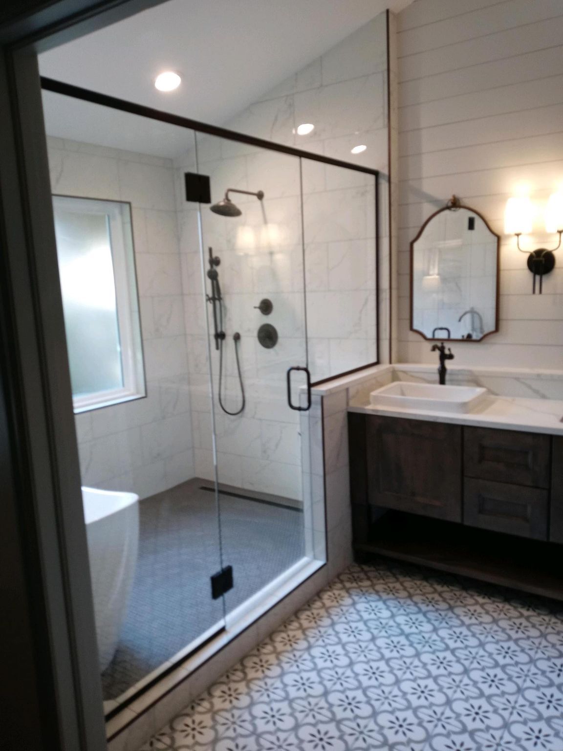 Modern bathroom with walk-in shower, vanity, and patterned tile flooring. Features black fixtures.