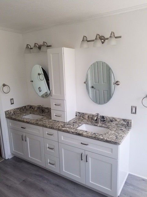 A bathroom with white cabinets , granite counter tops , a sink and a mirror.