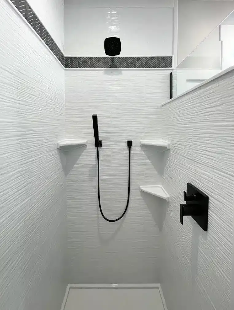 There is a shower with a black shower head and shelves.