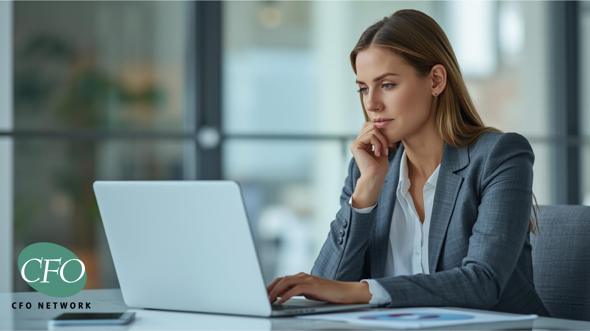 Woman in a grey suit, using a laptop, in a bright office setting. The CFO Network logo is in the corner.