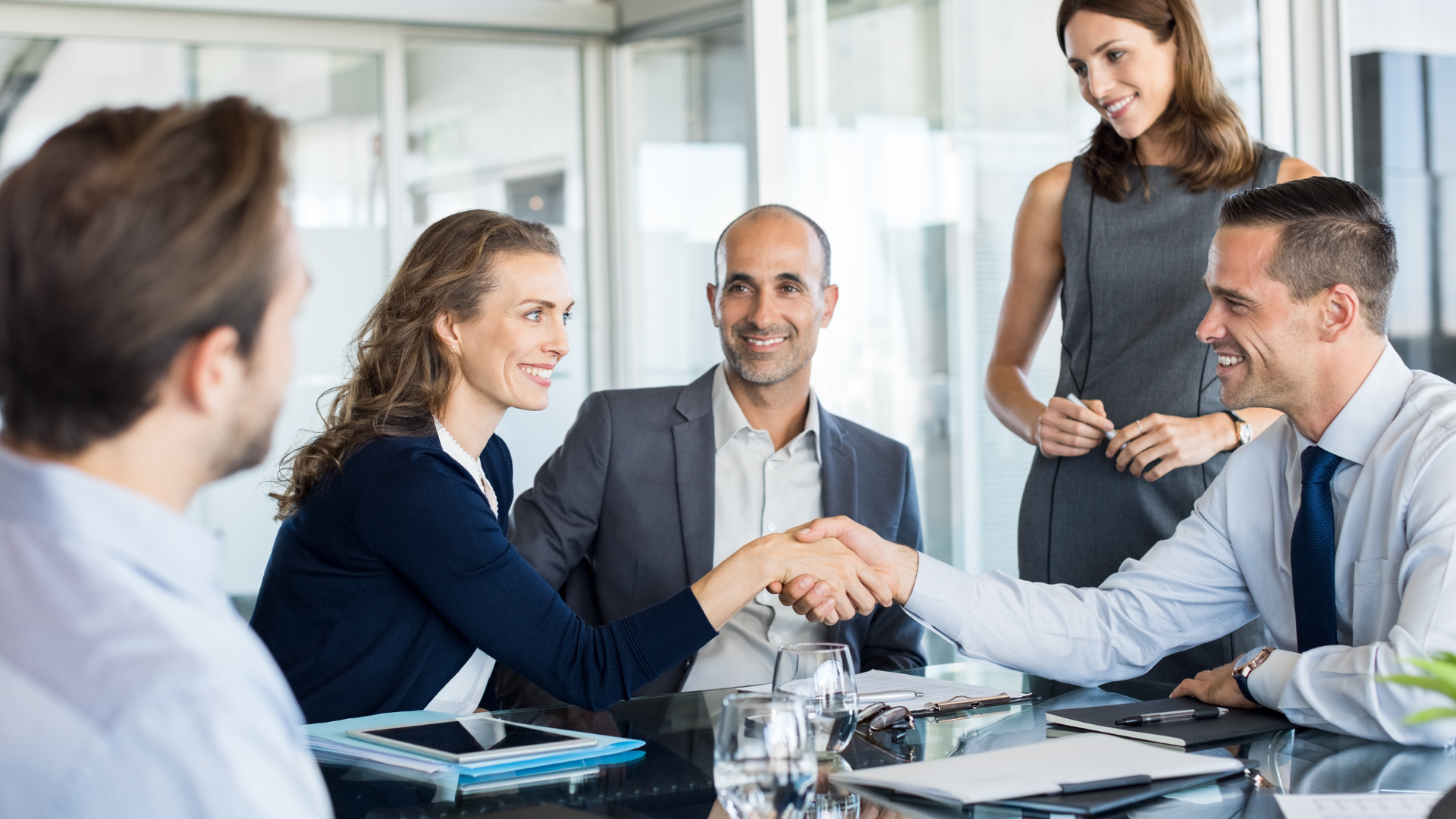 A group of business people are shaking hands while sitting around a table.