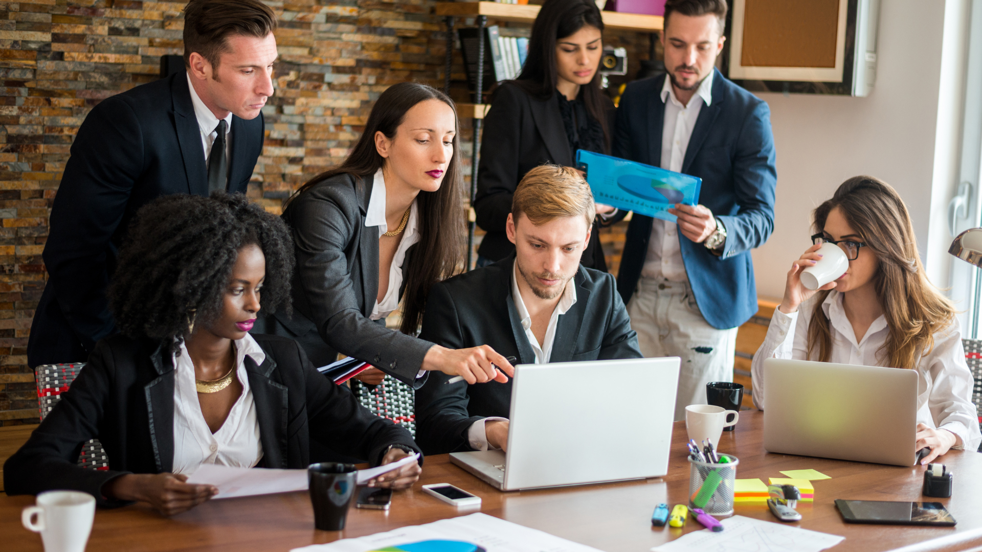 A group of business people are sitting around a table with laptops.