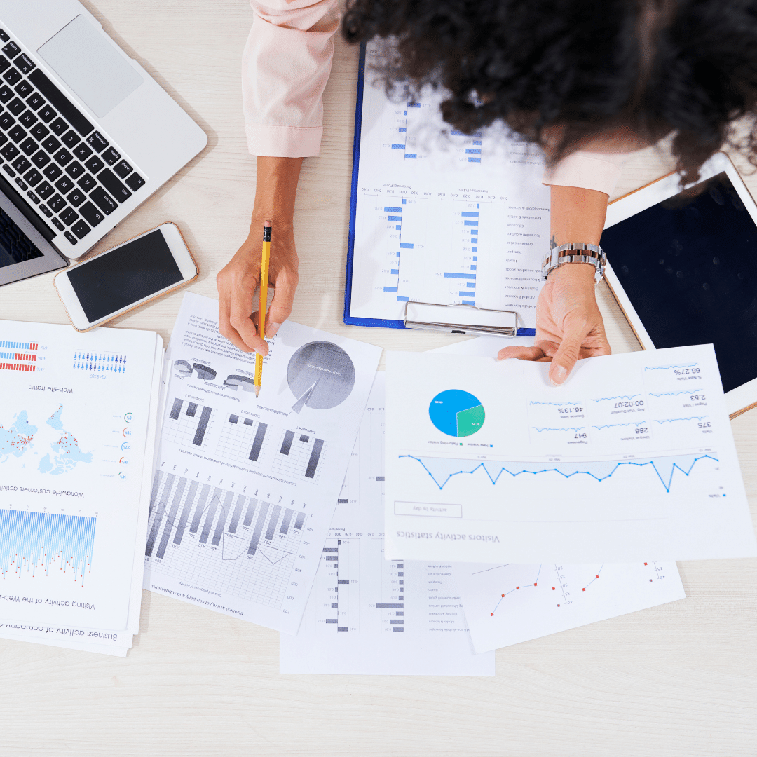 A woman is sitting at a desk looking at accounting graphs and a laptop.