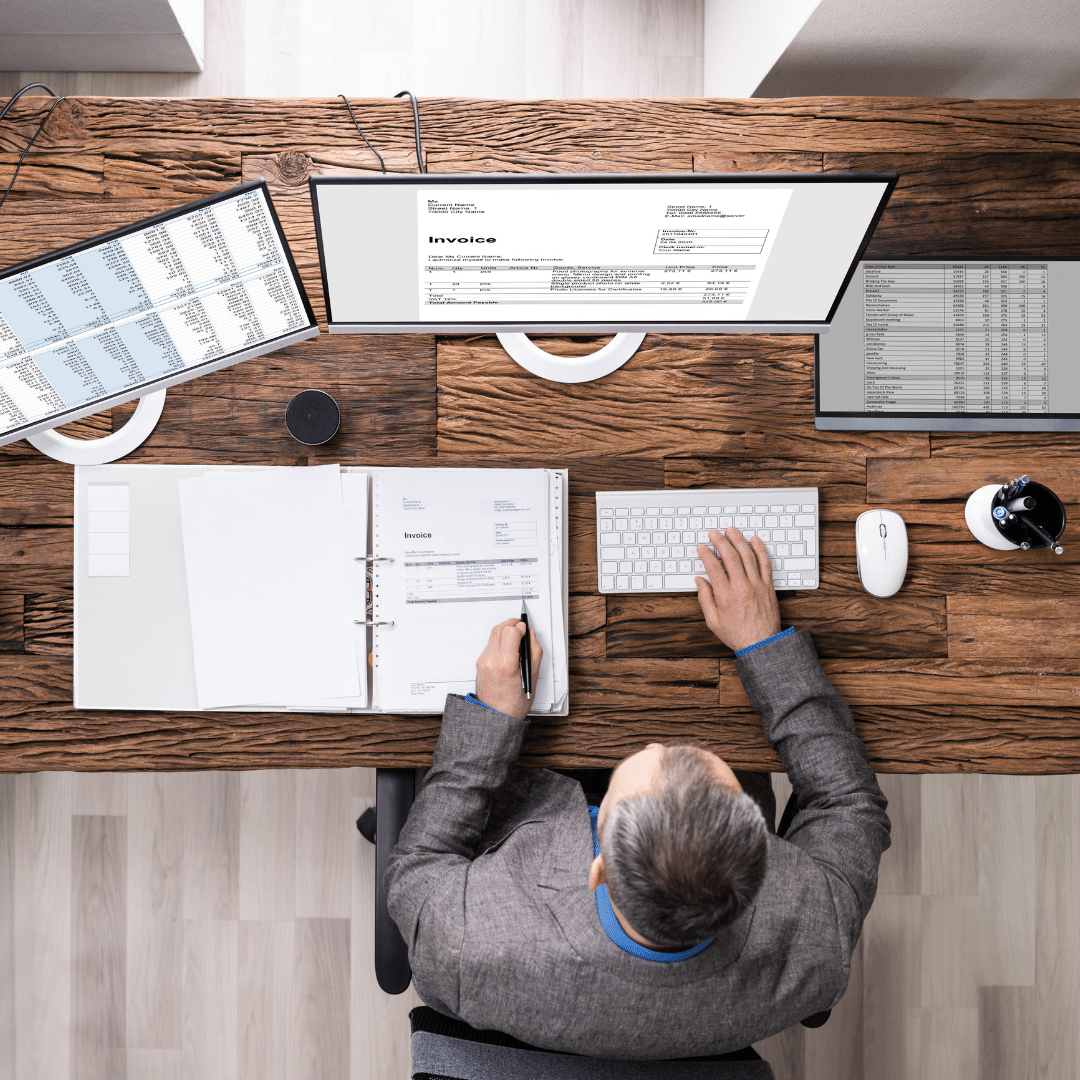 A man is sitting at a wooden desk working on a accounting issues.