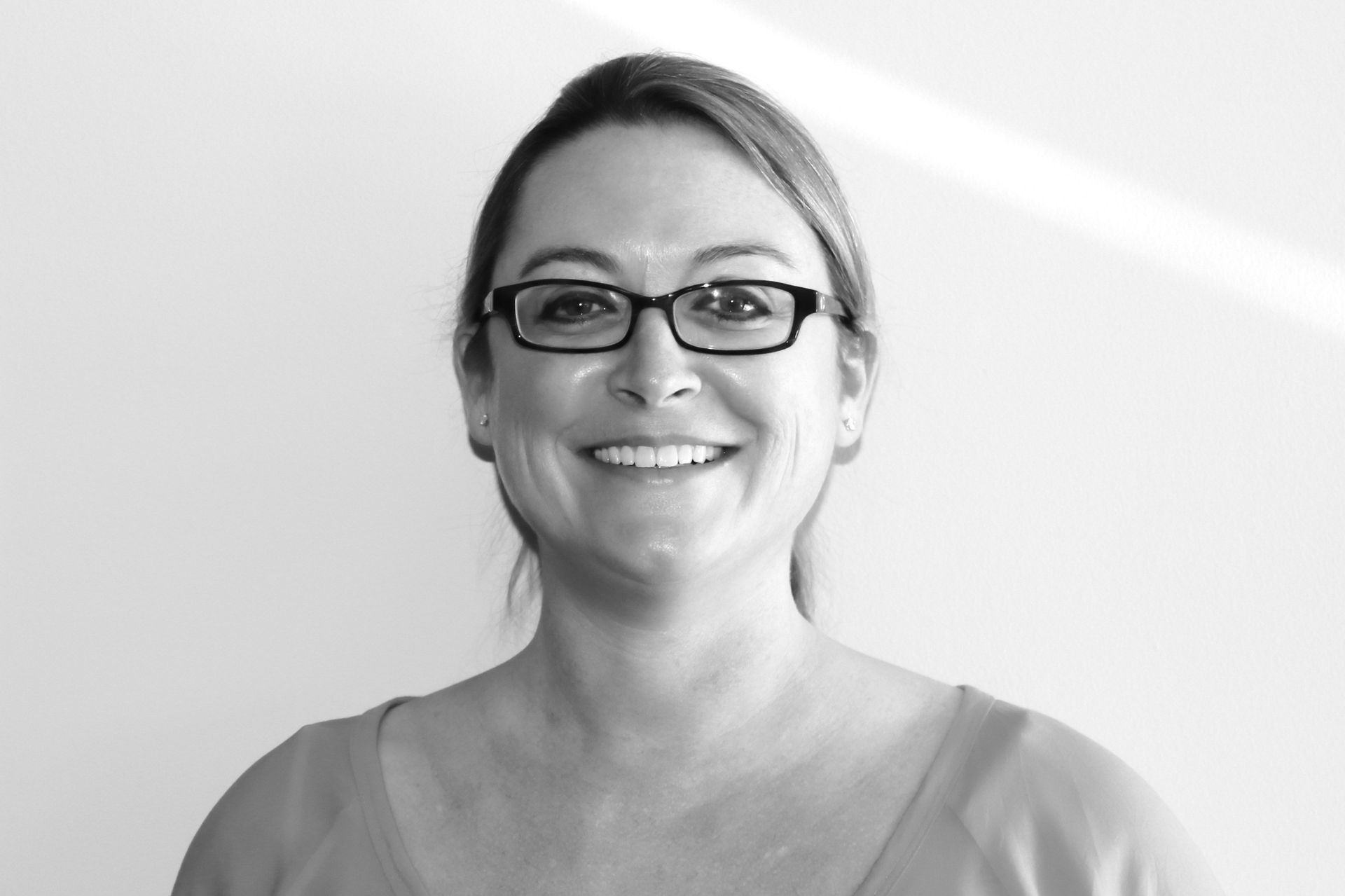 A woman wearing glasses is smiling in a black and white photo.