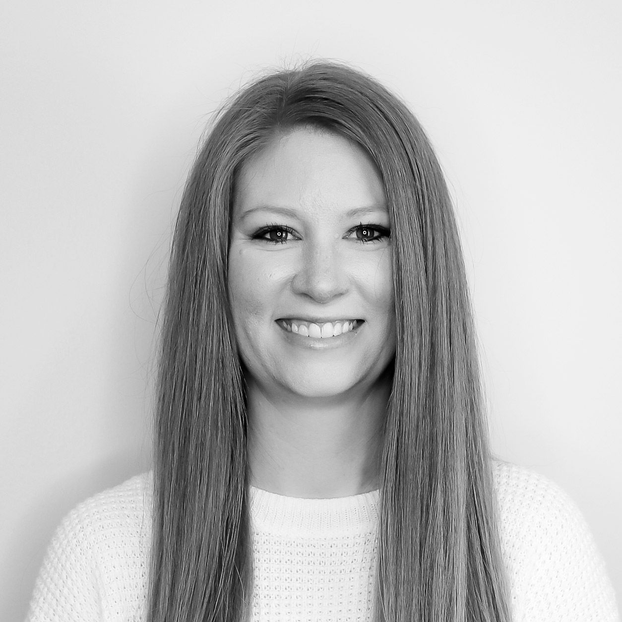 A woman with long hair is smiling in a black and white photo.